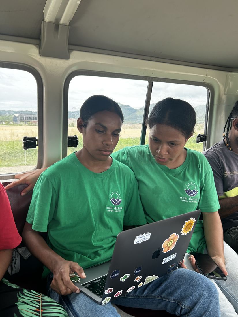 Two EcoScholars in Eda Davara shirts entering data on a laptop in a vehicle